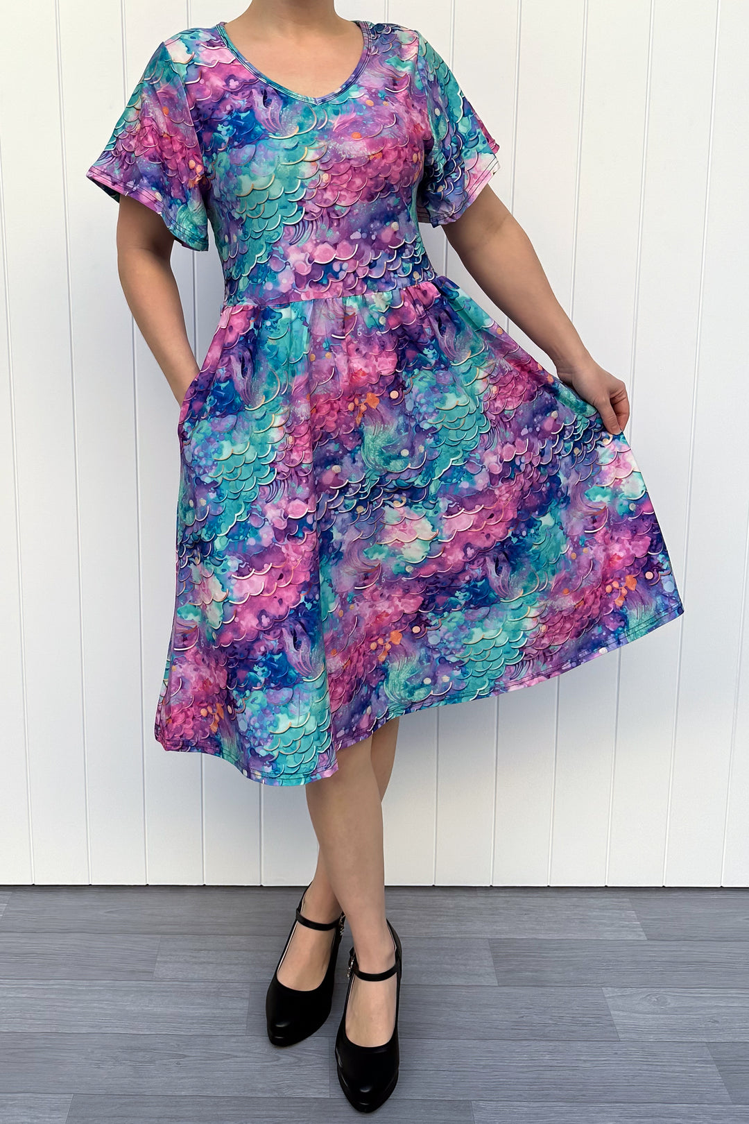 Person wearing a colourful mermaid fantasy pattern dress against a white wooden panel background