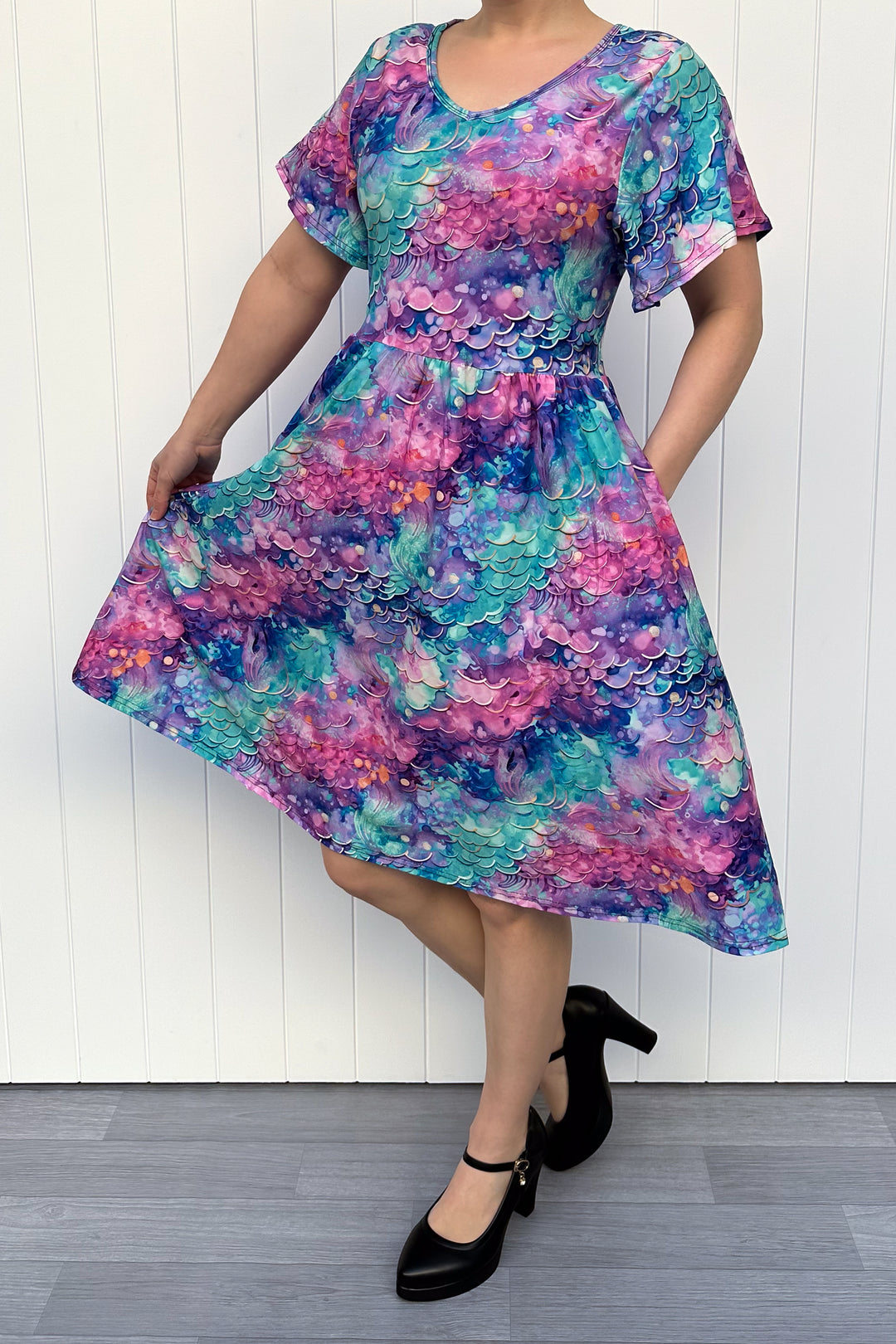 Person wearing a colourful mermaid fantasy pattern dress against a white wooden panel background