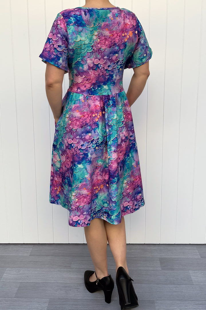Person wearing a colourful mermaid fantasy pattern dress against a white wooden panel background