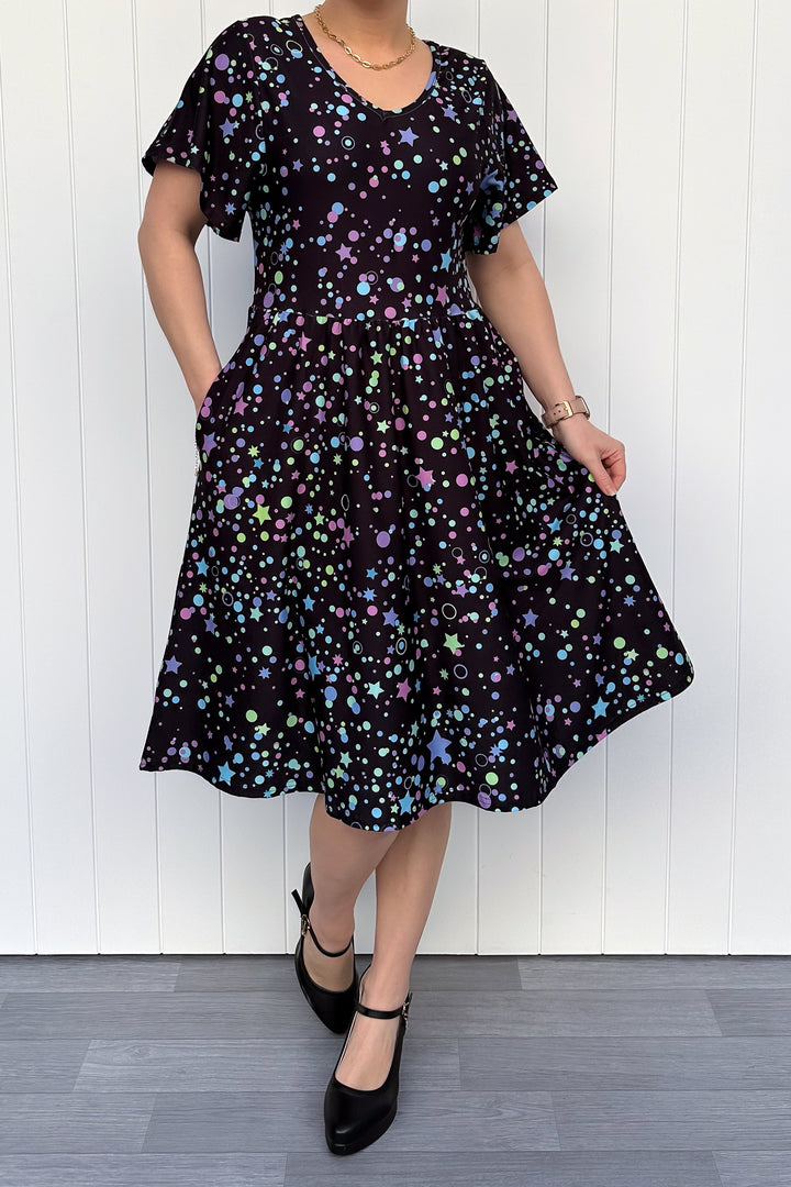 Person wearing a black dress with colorful star pattern against a white wooden panel background