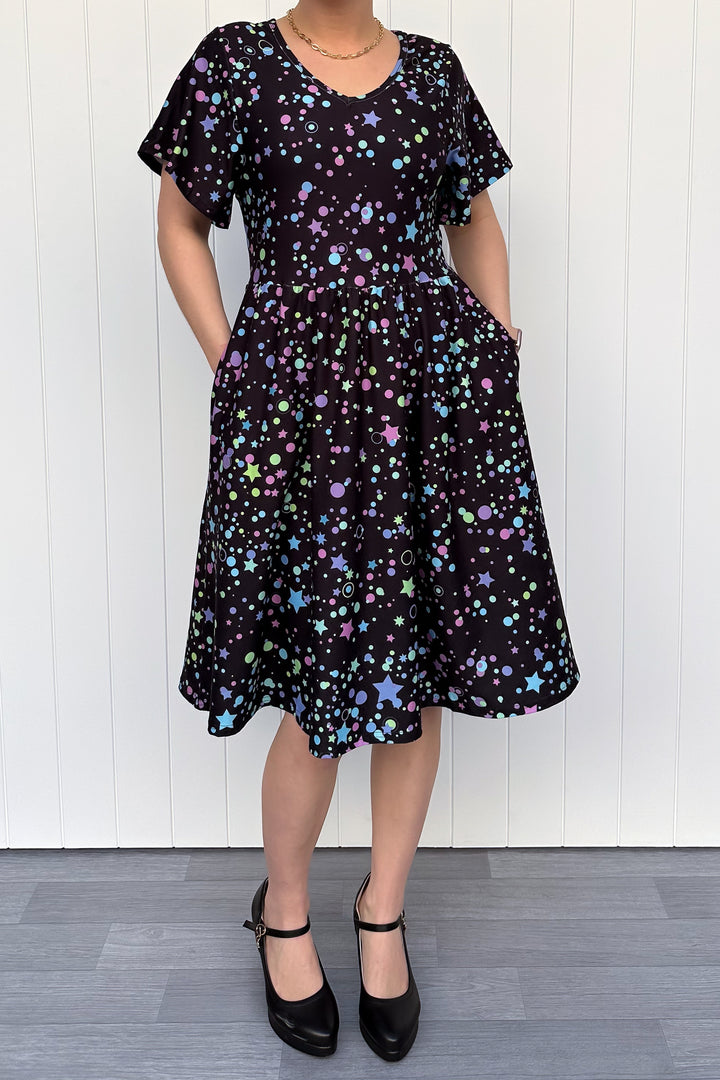 Person wearing a black dress with colorful star pattern against a white wall.