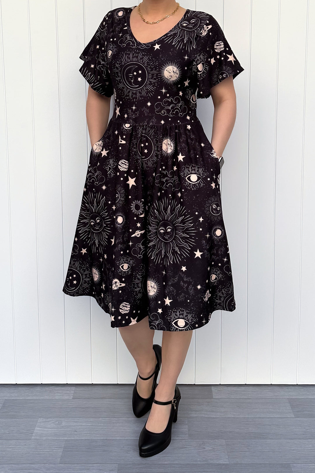 Person wearing a black dress with celestial pattern against a white wooden panel background
