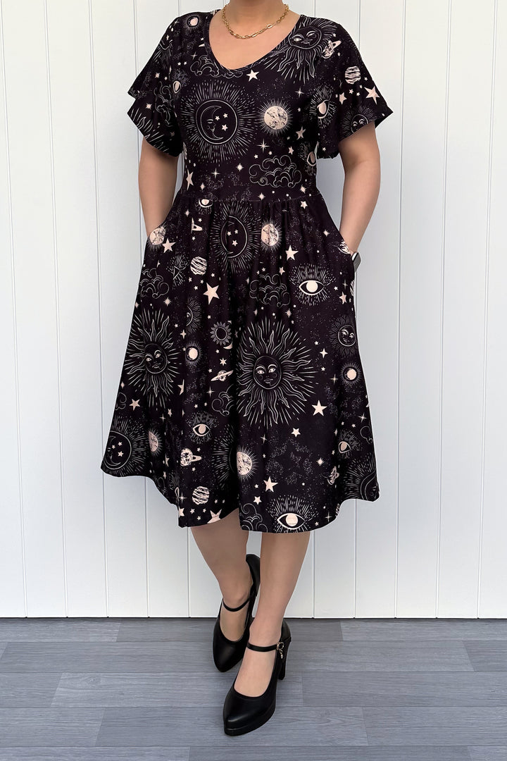 Person wearing a black dress with celestial pattern against a white wooden panel background
