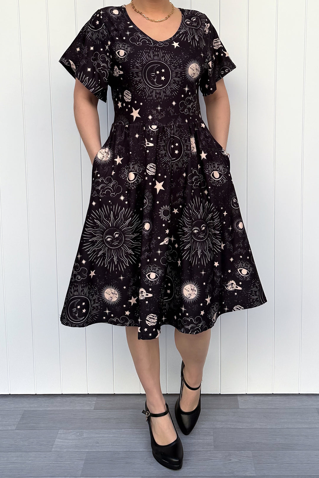 Person wearing a black dress with celestial pattern against a white wooden panel background