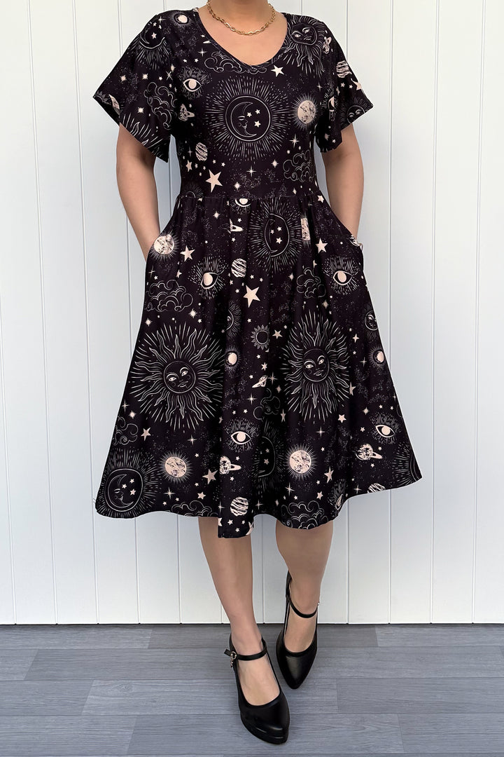 Person wearing a black dress with celestial pattern against a white wooden panel background