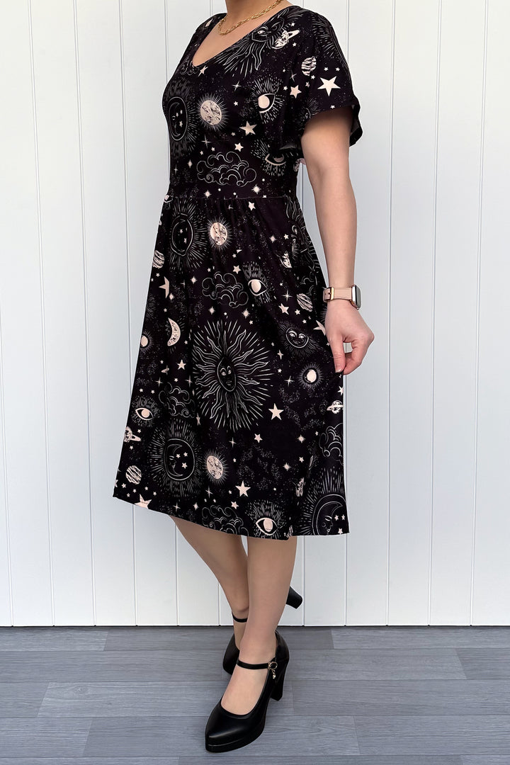 Person wearing a black dress with celestial pattern against a white wooden panel background