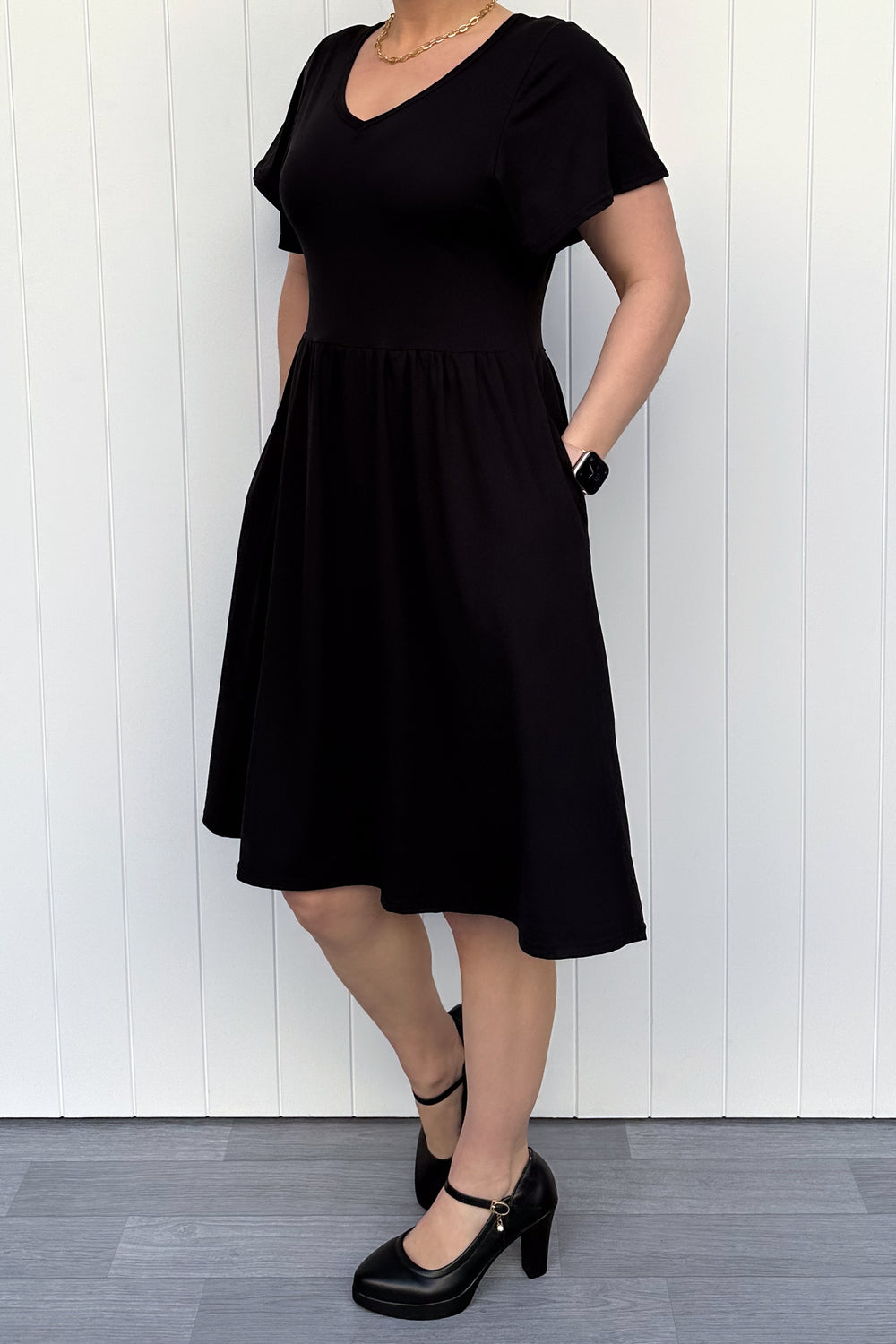 Person wearing a black dress standing against a white wooden panel background