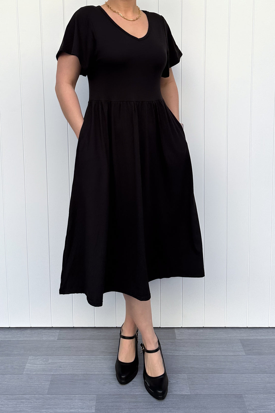 Person wearing a black dress standing against a white wooden panel background