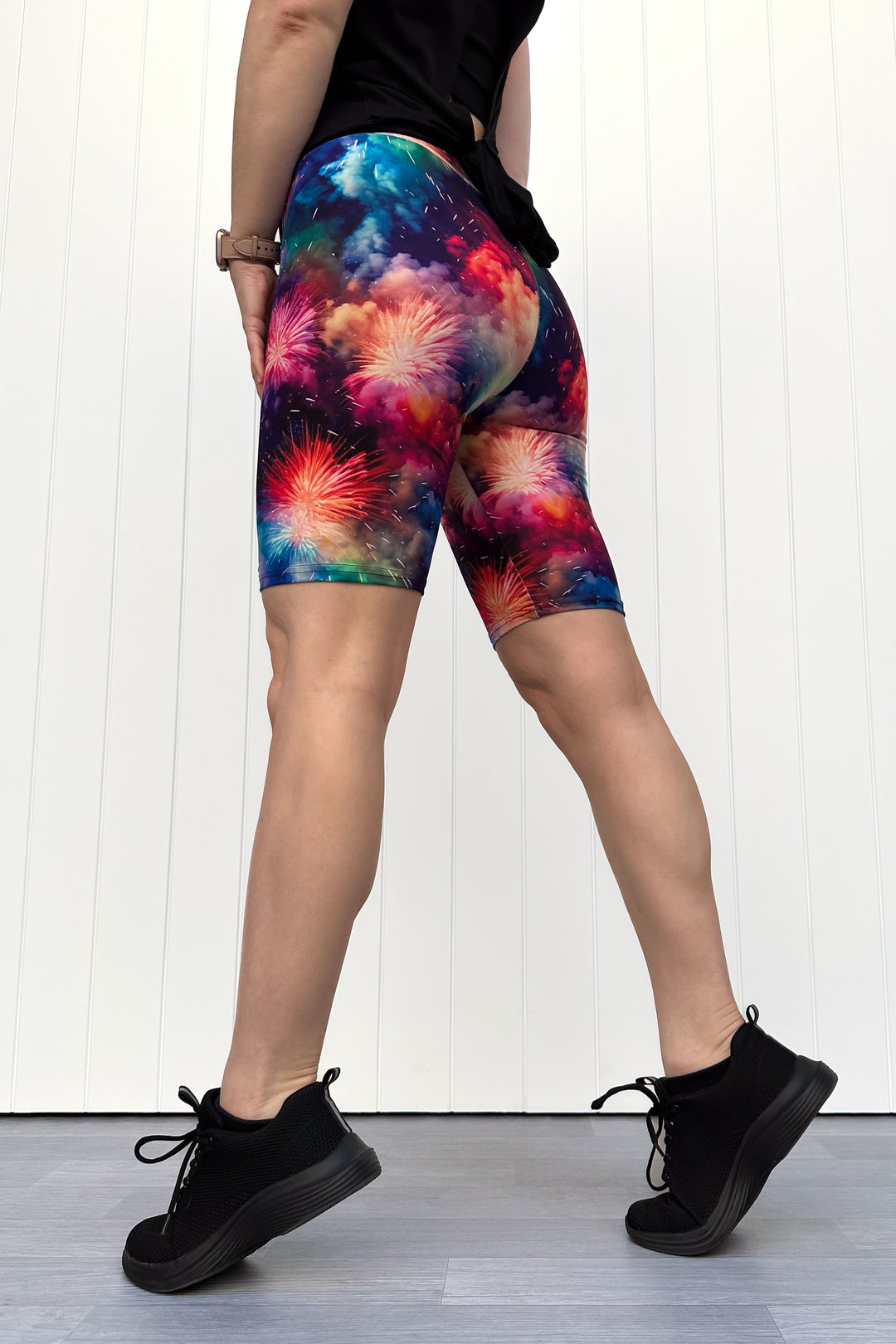 Person wearing colorful firework patterened shorts, standing against a white wall.