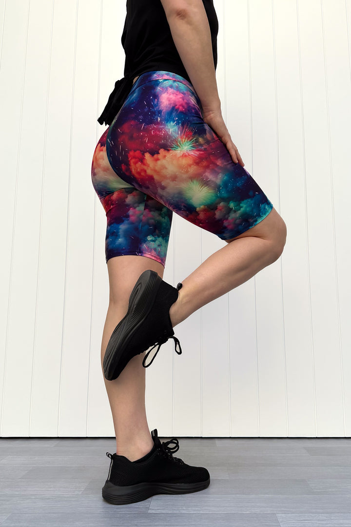 Person wearing colorful firework patterened shorts, standing against a white wall.