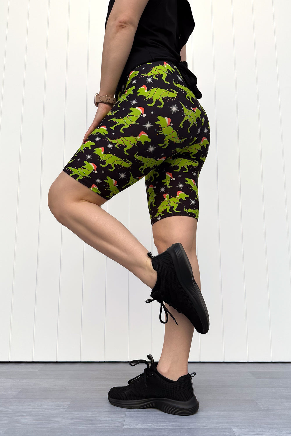 Person wearing shorts with green dinosaurs wearing santa hats on a black background.
