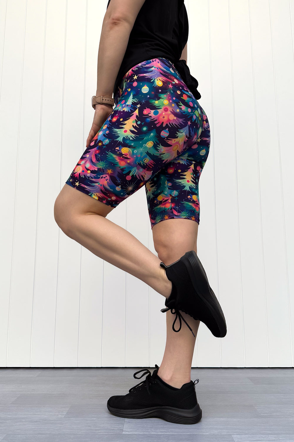 Person wearing shorts with a pattern of colourful Christmas trees against a white wooden panel background.