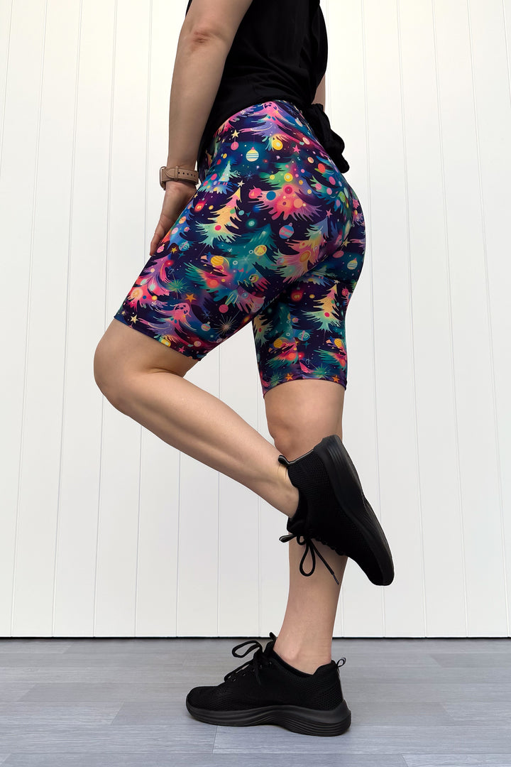Person wearing shorts with a pattern of colourful Christmas trees against a white wooden panel background.