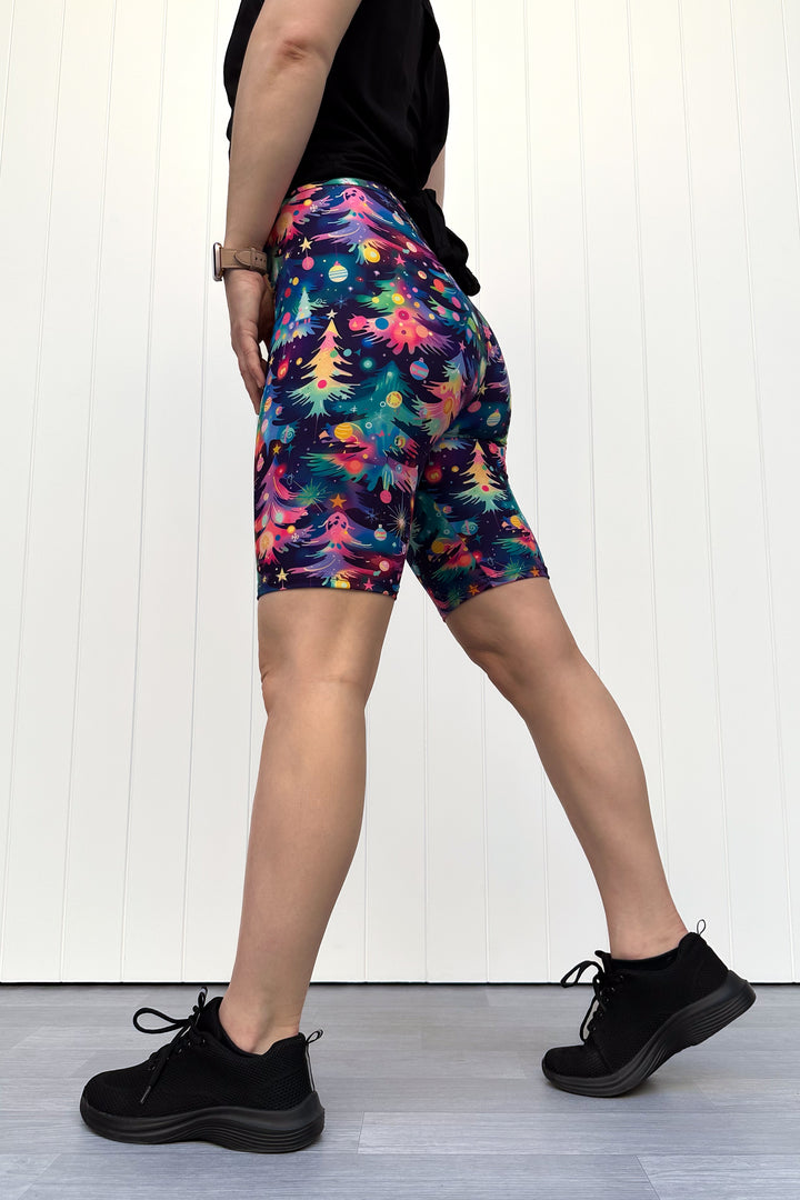 Person wearing shorts with a pattern of colourful Christmas trees against a white wooden panel background.