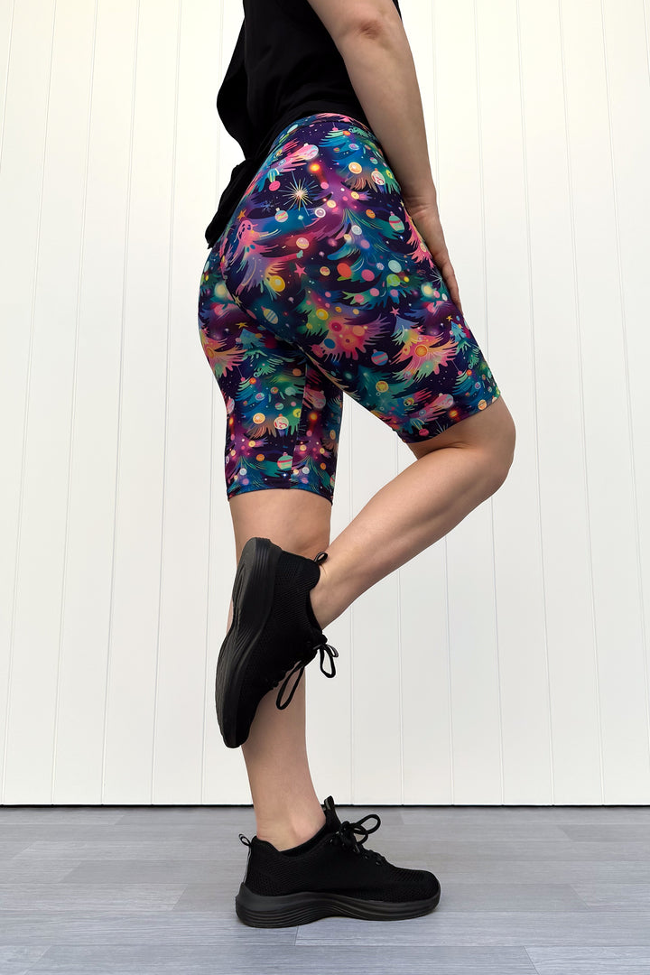 Person wearing shorts with a pattern of colourful Christmas trees against a white wooden panel background.