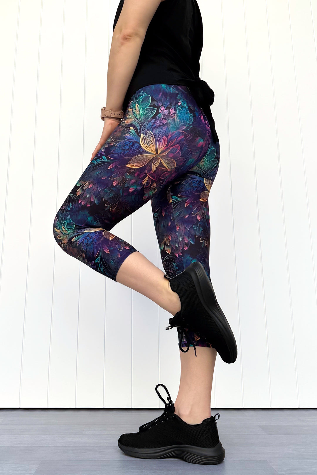 Person wearing a black top and purple floral leggings against a white background