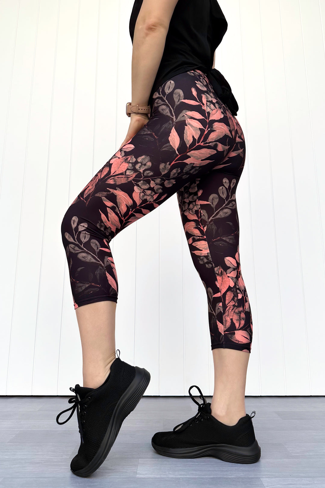 Person wearing black leggings with floral pattern and black sneakers on a white background