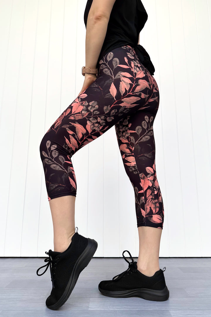 Person wearing black leggings with floral pattern and black sneakers on a white background