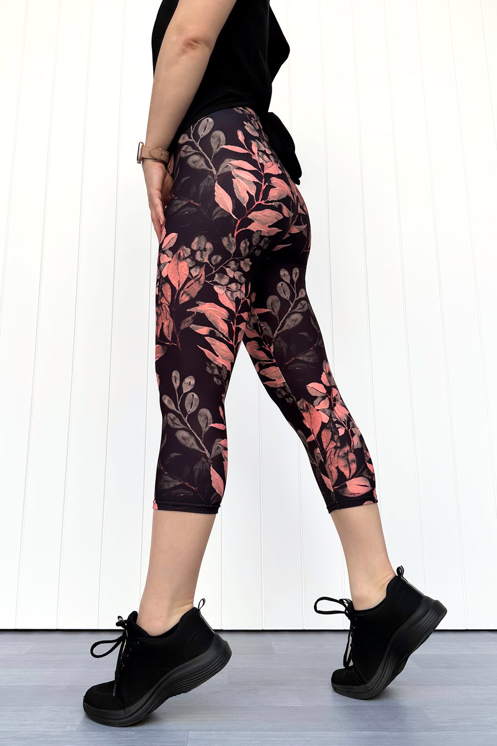 Person wearing black leggings with pink floral pattern and black sneakers on a white background
