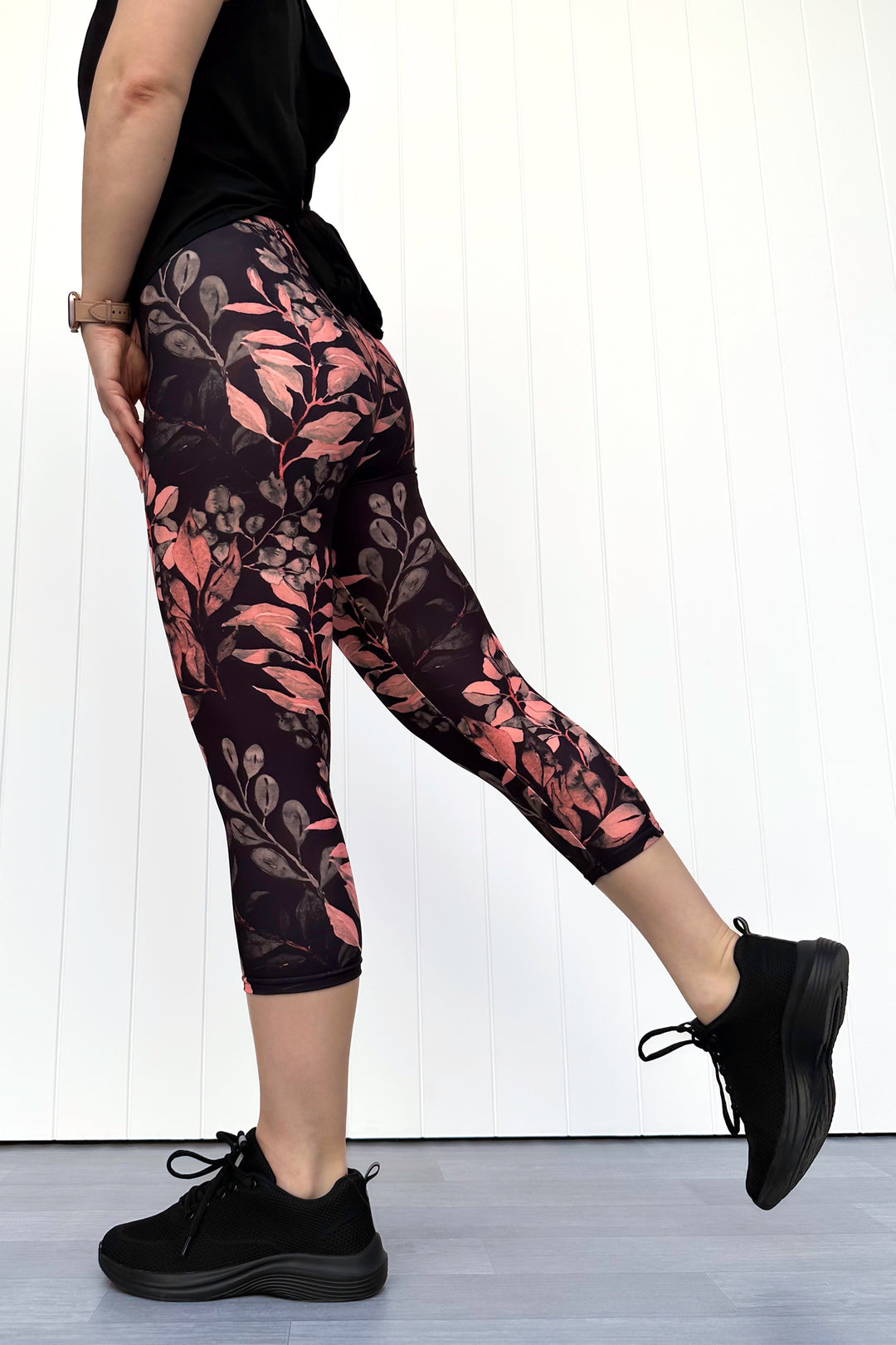 Person wearing black leggings with floral pattern and black sneakers on a white background