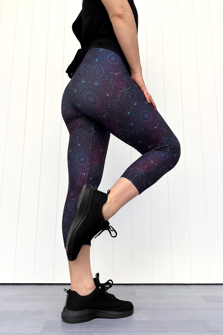 Person wearing dark purple mandala patterned leggings and black sneakers on a white background