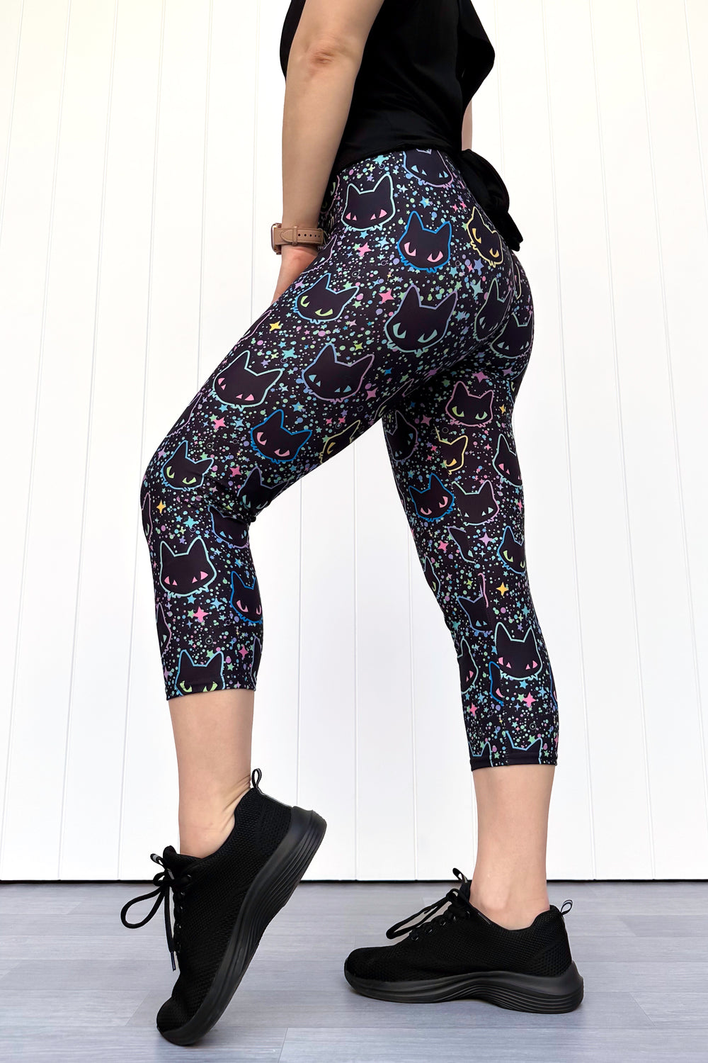 Person wearing black leggings with cat pattern and black shoes on a white background