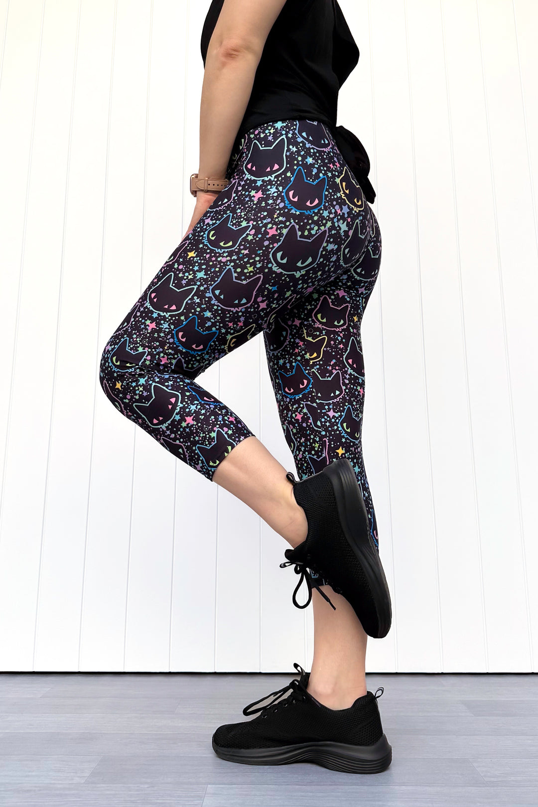 Person wearing black leggings with cat pattern and black shoes on a white background