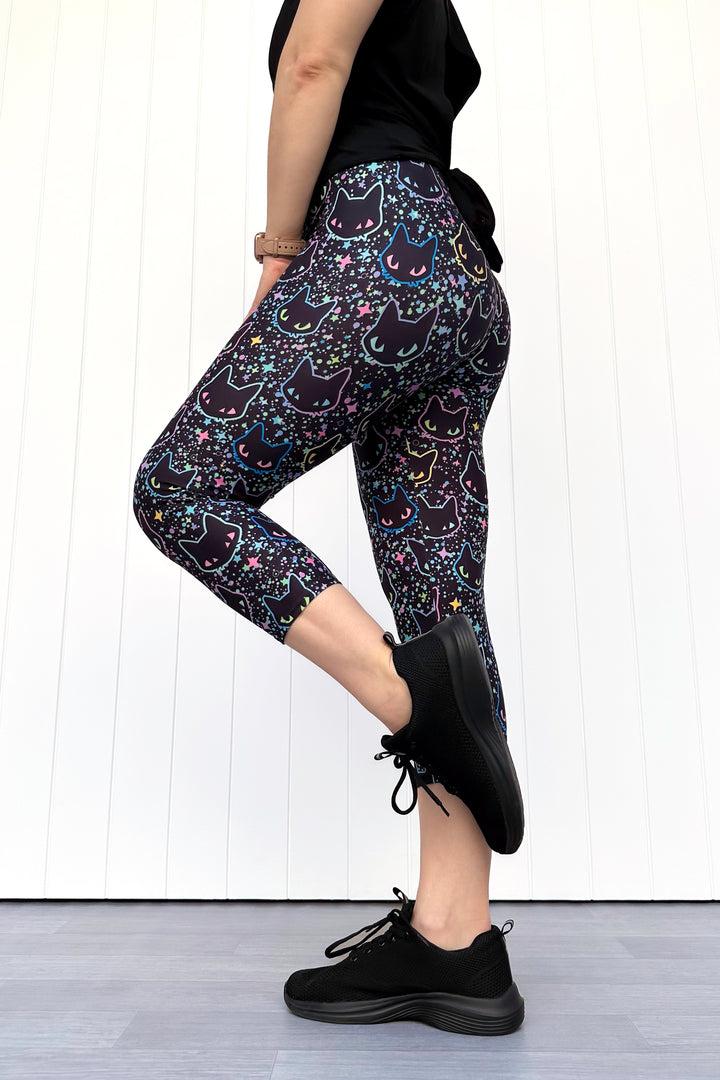 Person wearing black leggings with cat pattern and black shoes on a white background