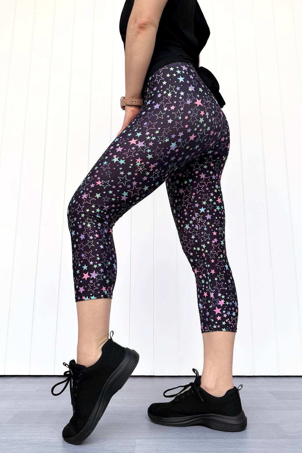 Person wearing black leggings with star pattern and black sneakers on a white background