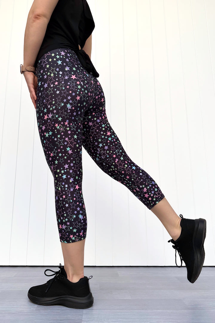Person wearing black leggings with star pattern and black shoes on a white background