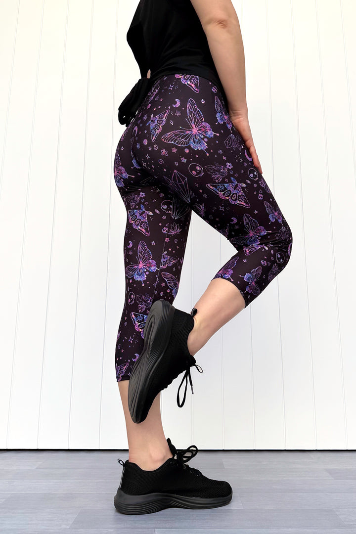 Person wearing purple butterfly-patterned leggings and black sneakers on a white background