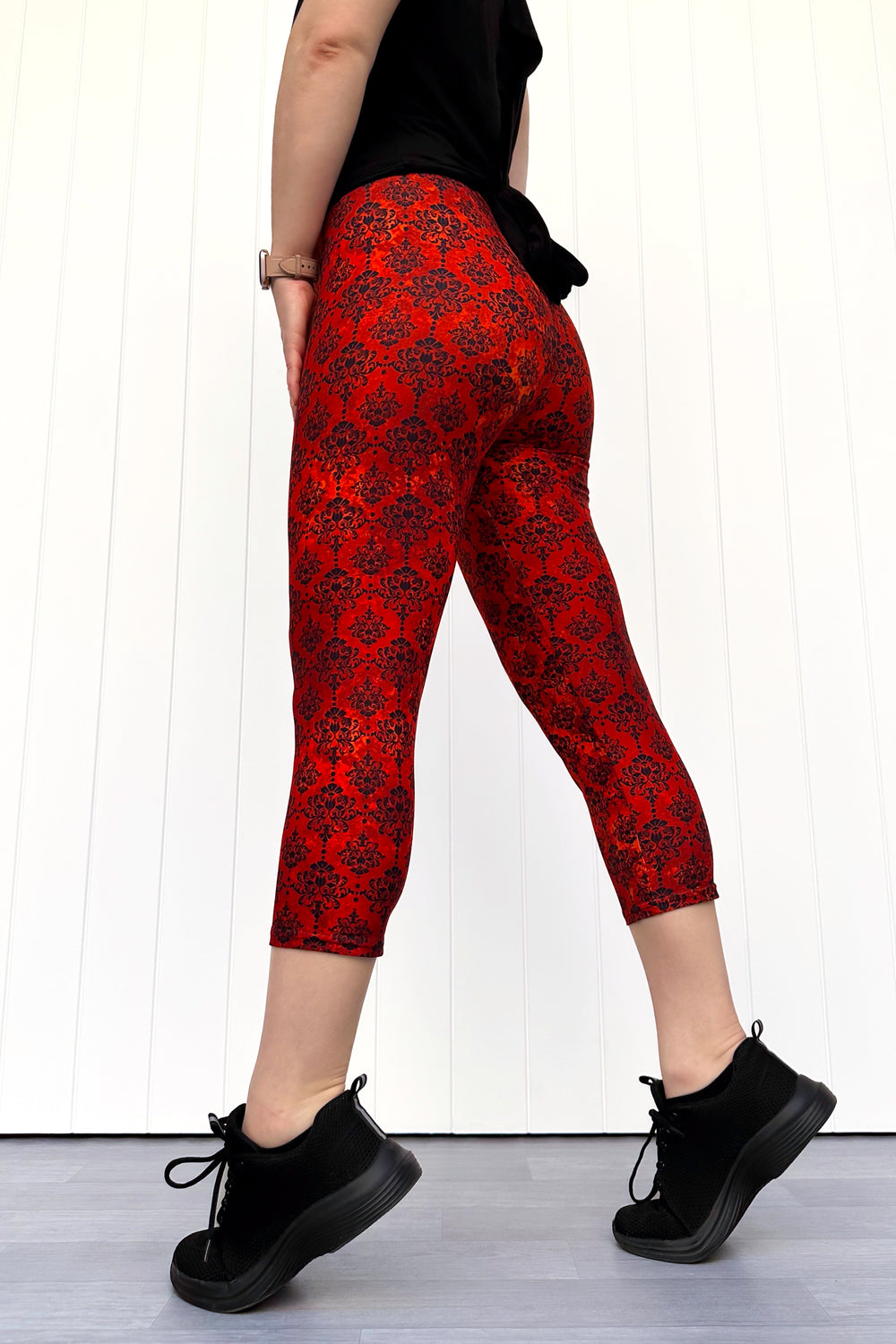 Person wearing red patterned leggings and black shoes on a white background
