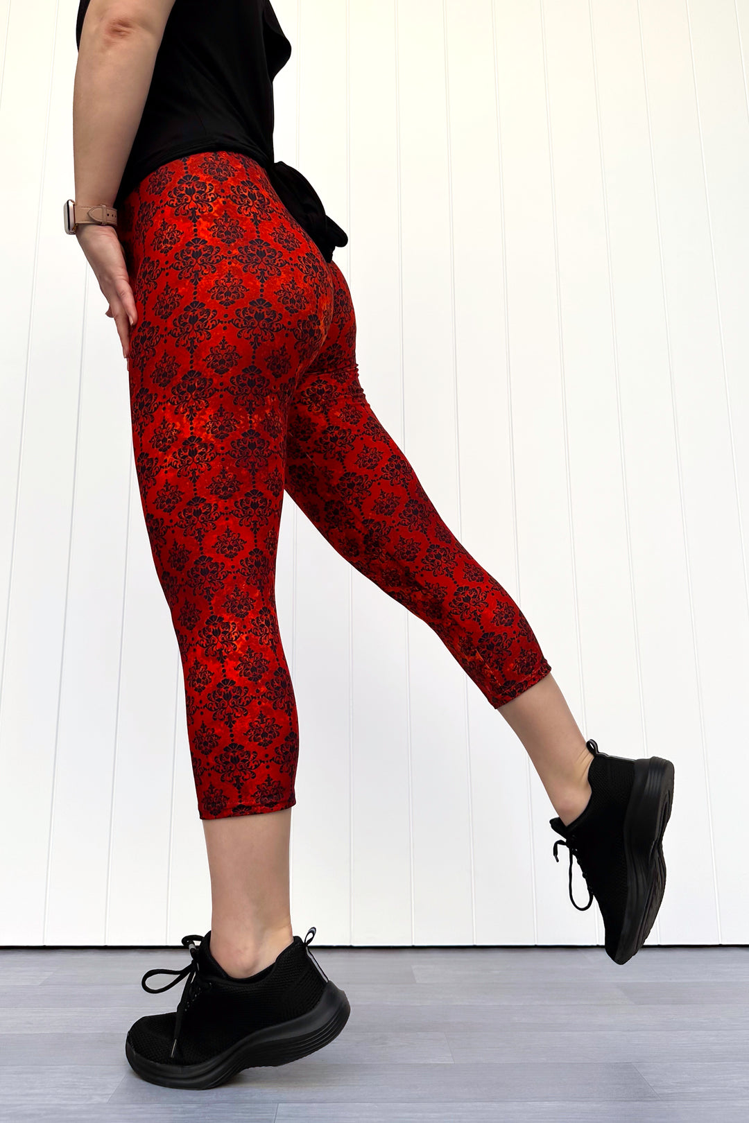 Person wearing red patterned leggings and black shoes on a white background