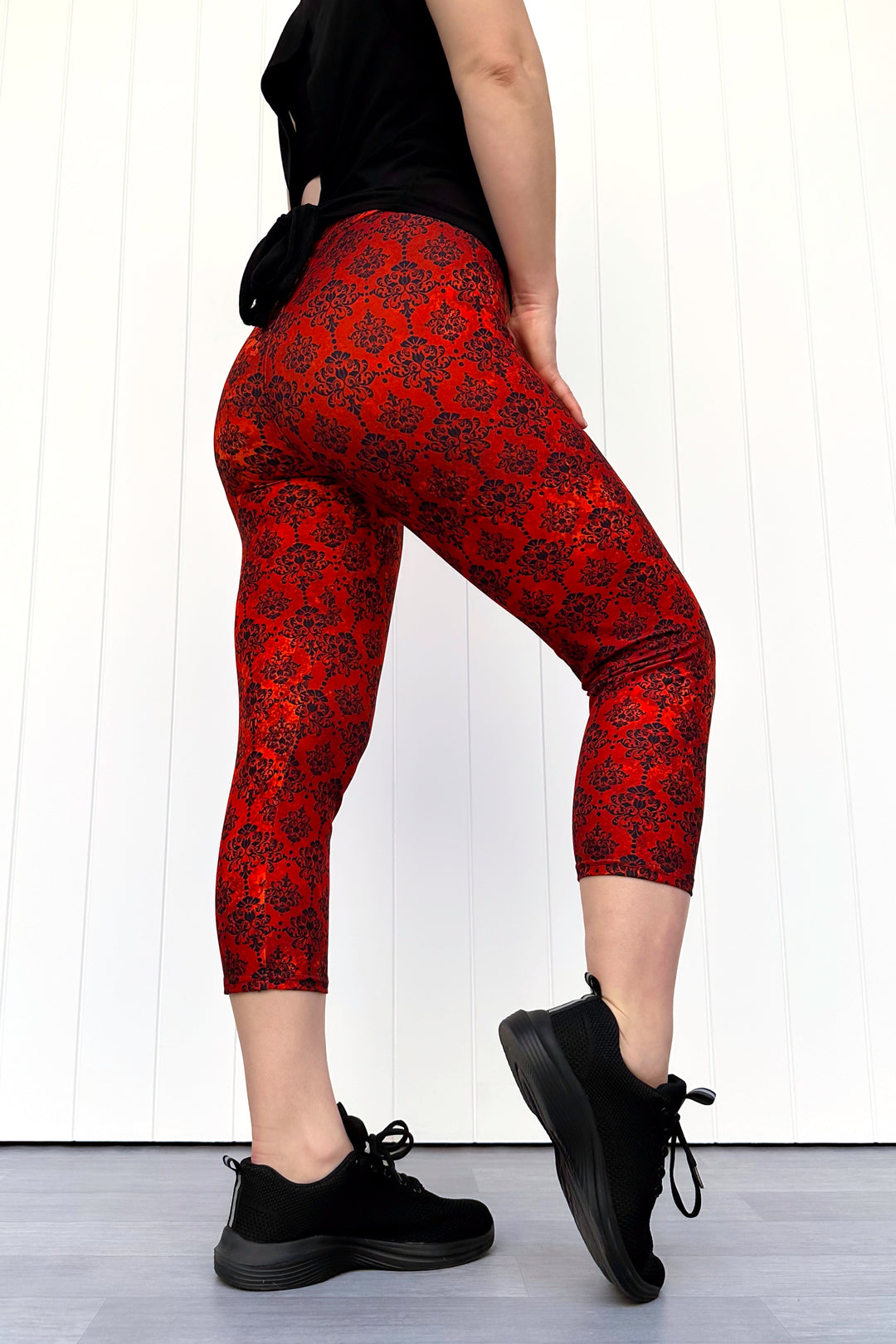 Person wearing red patterned leggings and black shoes on a white background