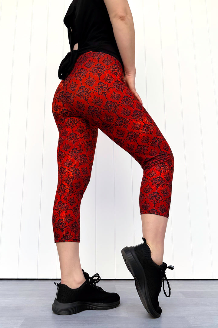 Person wearing red patterned leggings and black shoes on a white background
