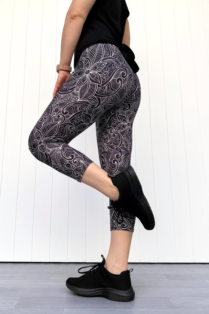 Person wearing black and white patterned leggings with black shoes on a white wooden floor.