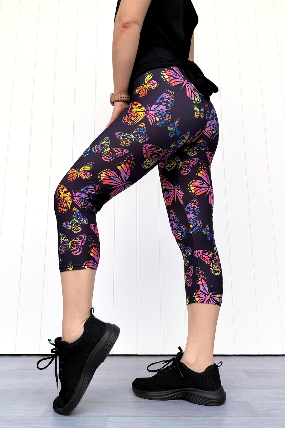 Person wearing black leggings with colorful butterfly pattern and black sneakers on a white background