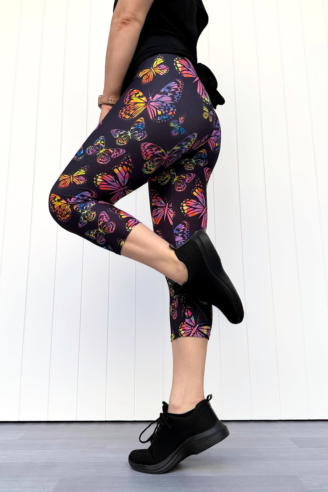 Person wearing black leggings with colorful butterfly pattern on a white background