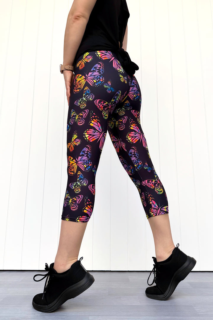 Person wearing black leggings with colorful butterfly pattern and black shoes on a white background