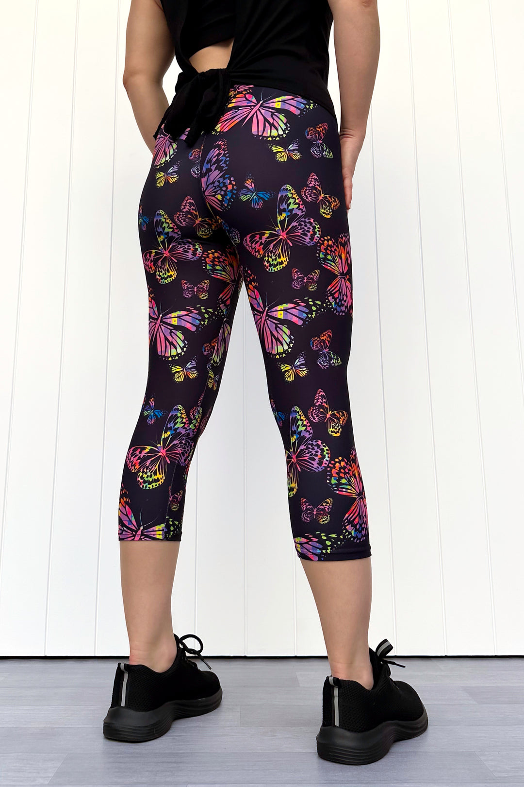 Person wearing black leggings with colorful butterfly pattern against a white background