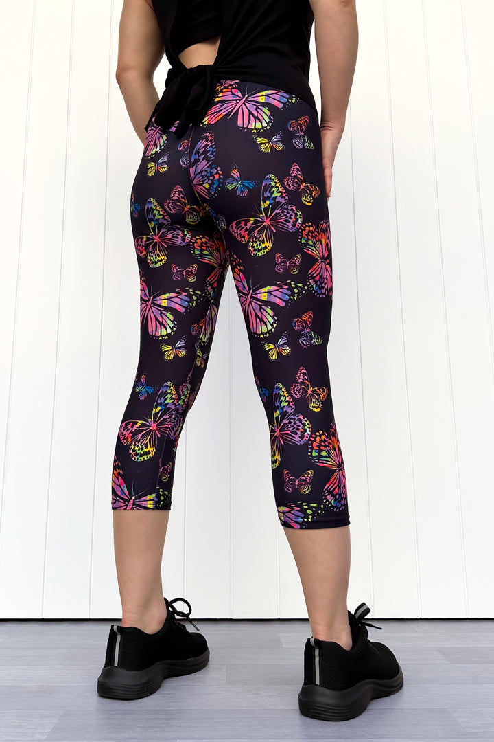 Person wearing black leggings with colorful butterfly pattern against a white background