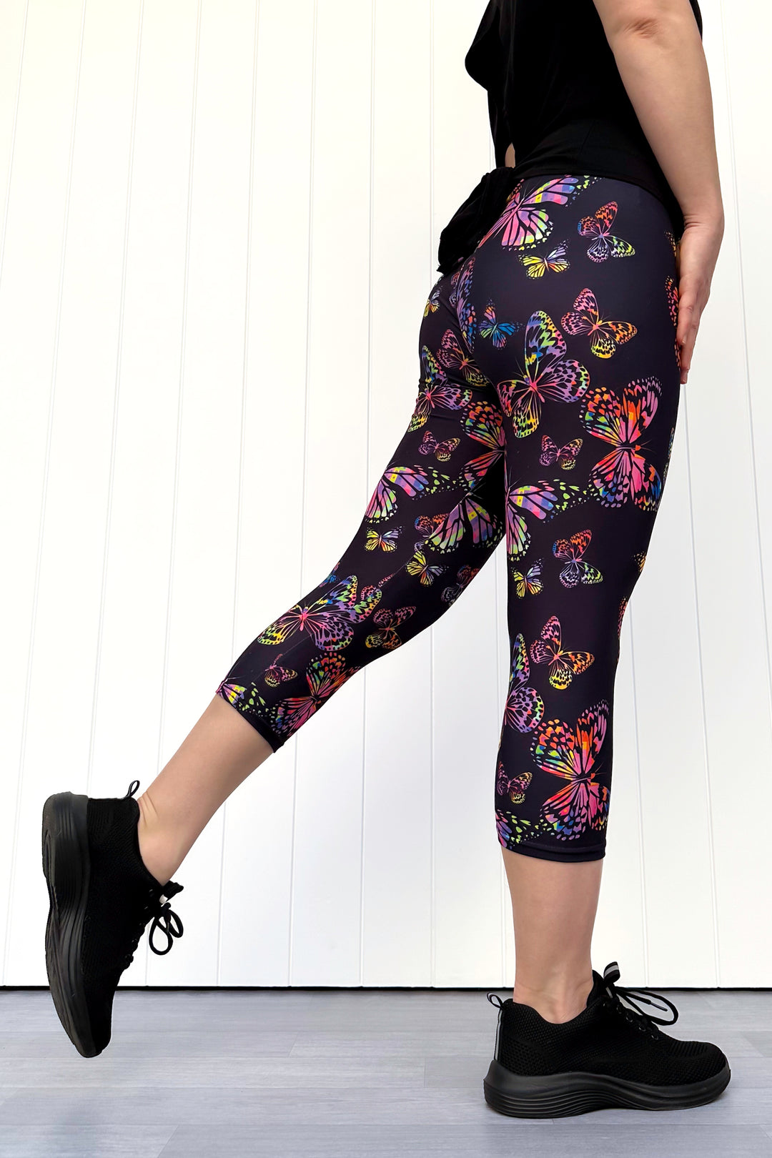 Person wearing black leggings with colorful butterfly pattern on a white background