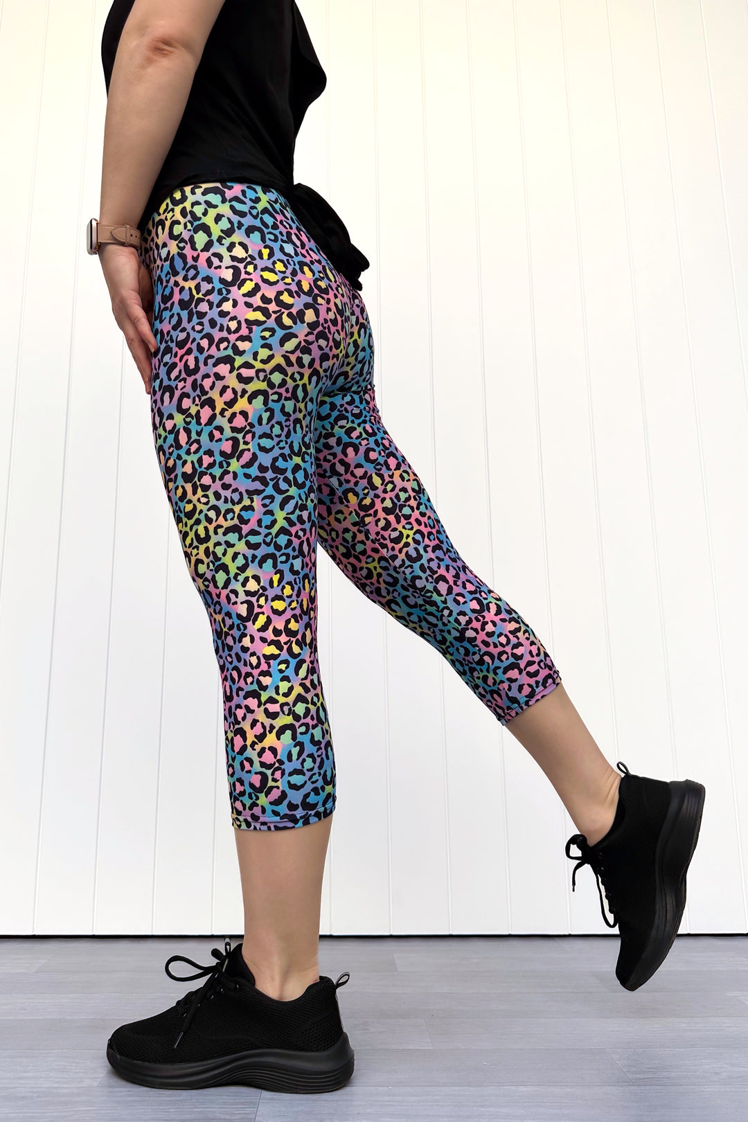 Person wearing colorful leopard print leggings with black shoes on a white background
