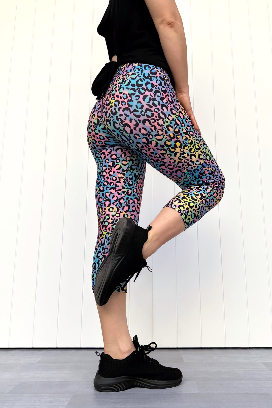 Person wearing colorful leopard print leggings with black shoes on a white background