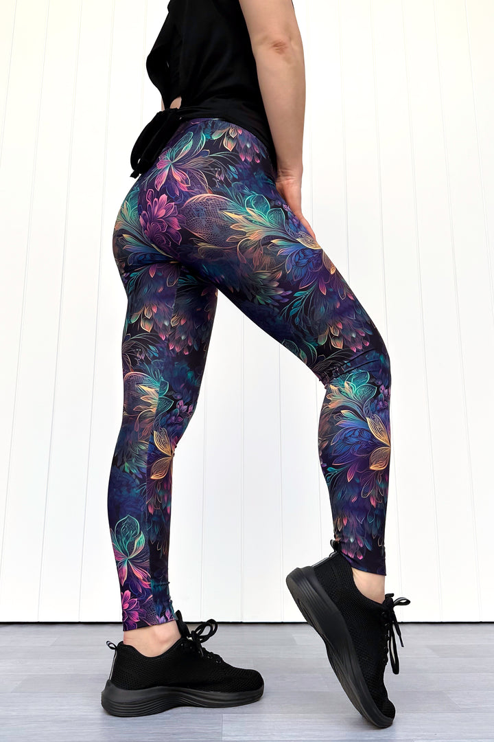 Person wearing colorful floral leggings with a black top and shoes on a white background