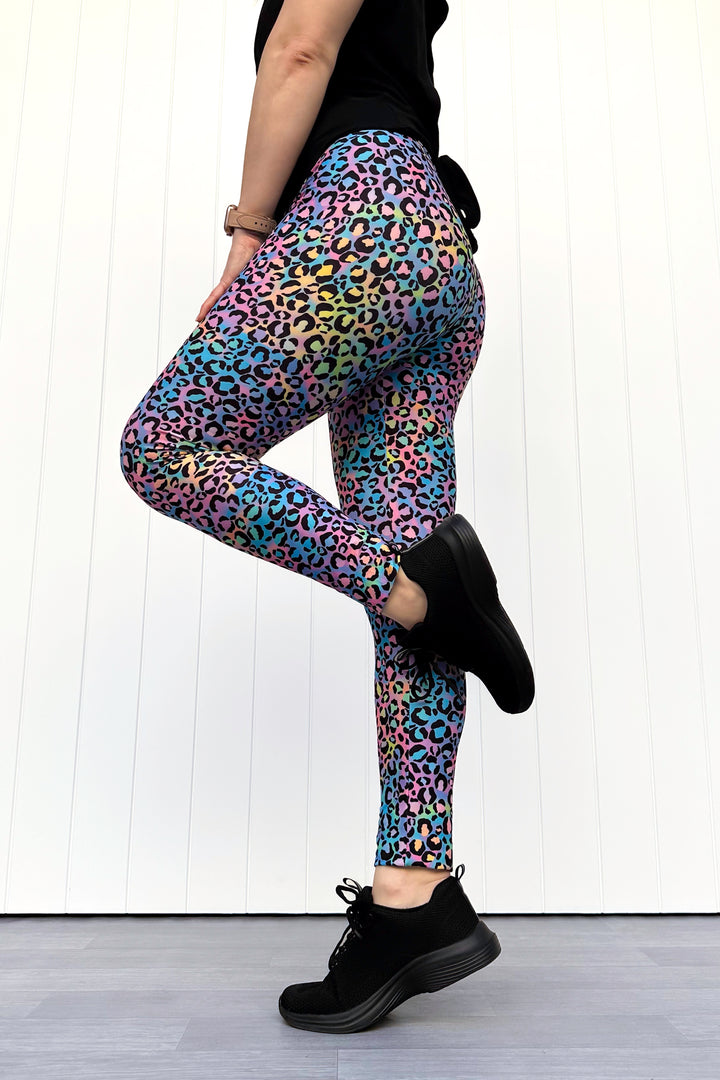 Person wearing colorful leopard print leggings and black shoes on a white wooden floor.