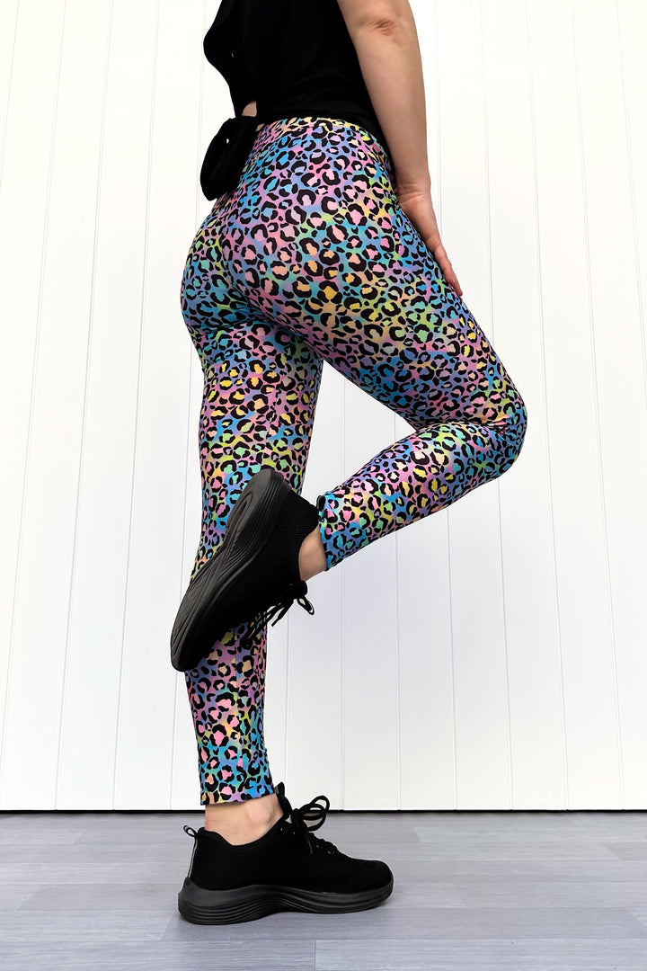 Person wearing colorful leopard print leggings with black shoes on a white background