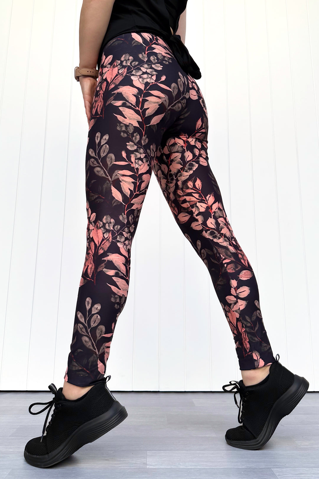 Person wearing black leggings with floral pattern against a white background
