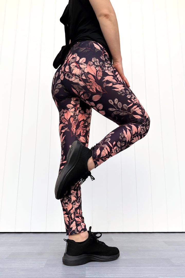 Person wearing black leggings with floral pattern and black sneakers on a white background