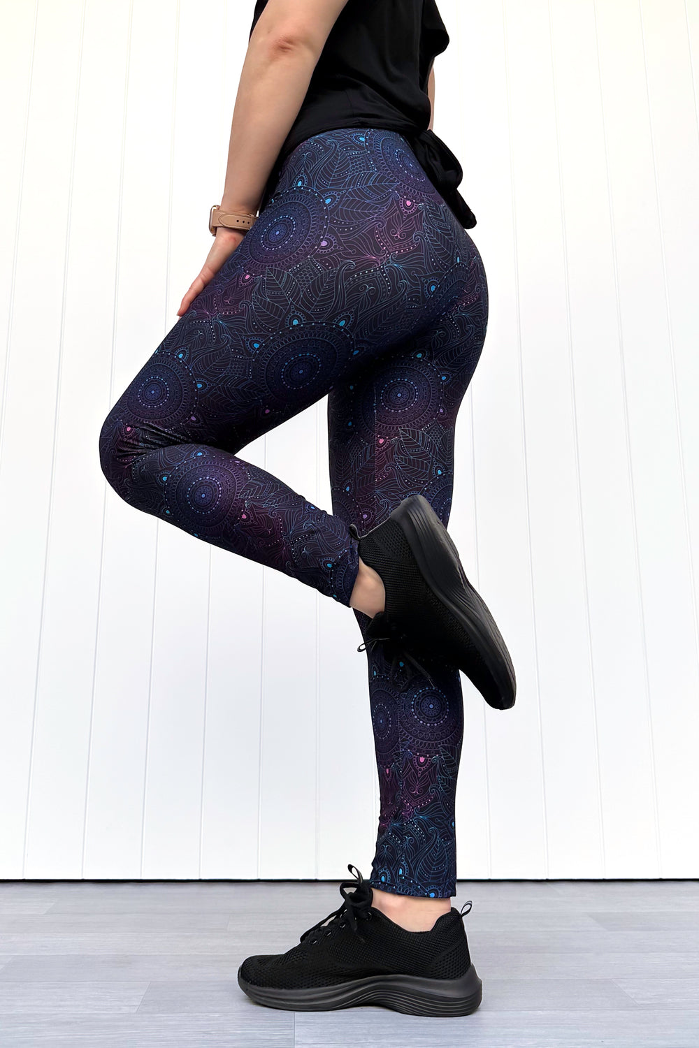 Person wearing dark blue mandala patterned leggings and black shoes on a white wooden floor.